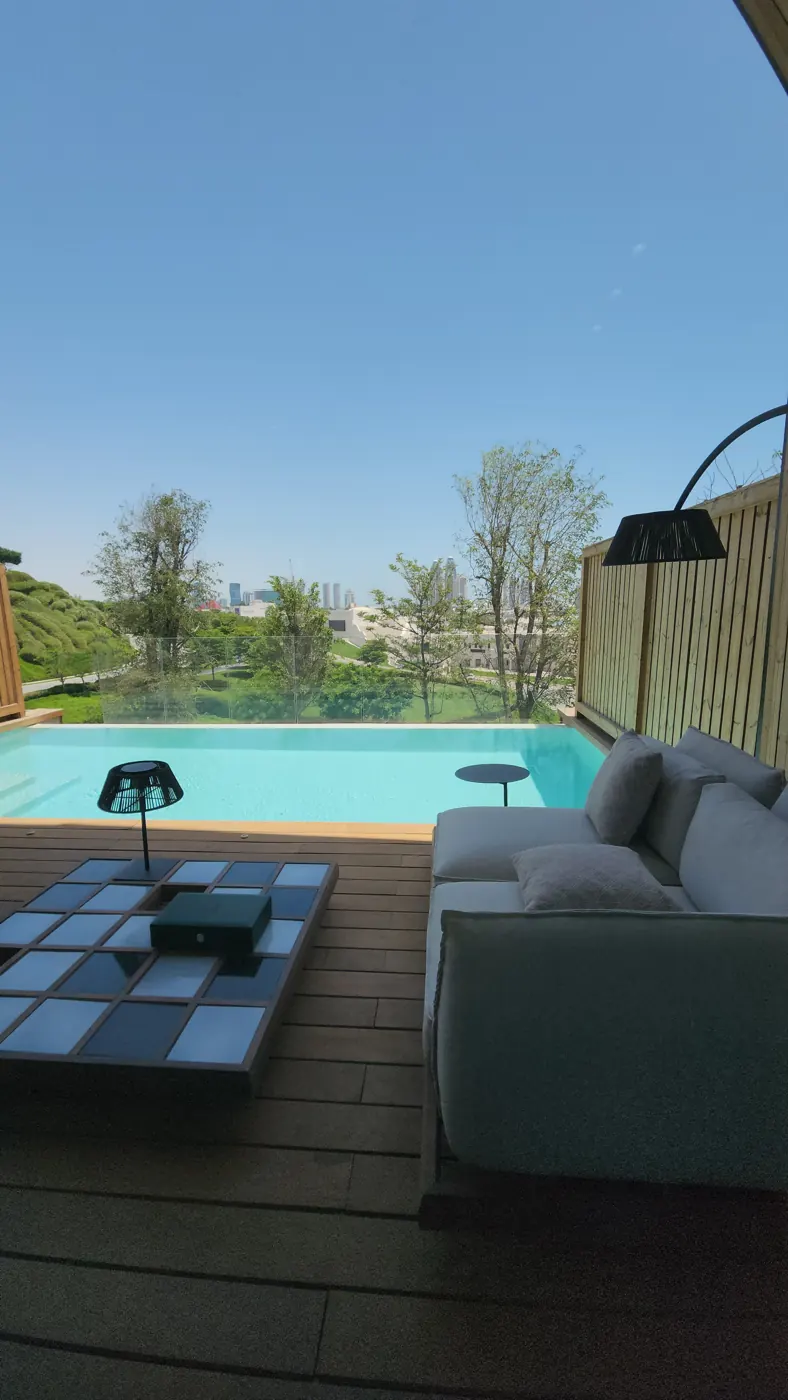 The private pool and terrace with a lounge seat and low table, looking out over green hills and the Doha skyline