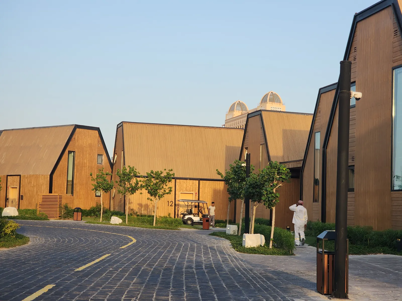 Wood-clad Katara Hills villas glowing in late-afternoon light along a stone-paved lane