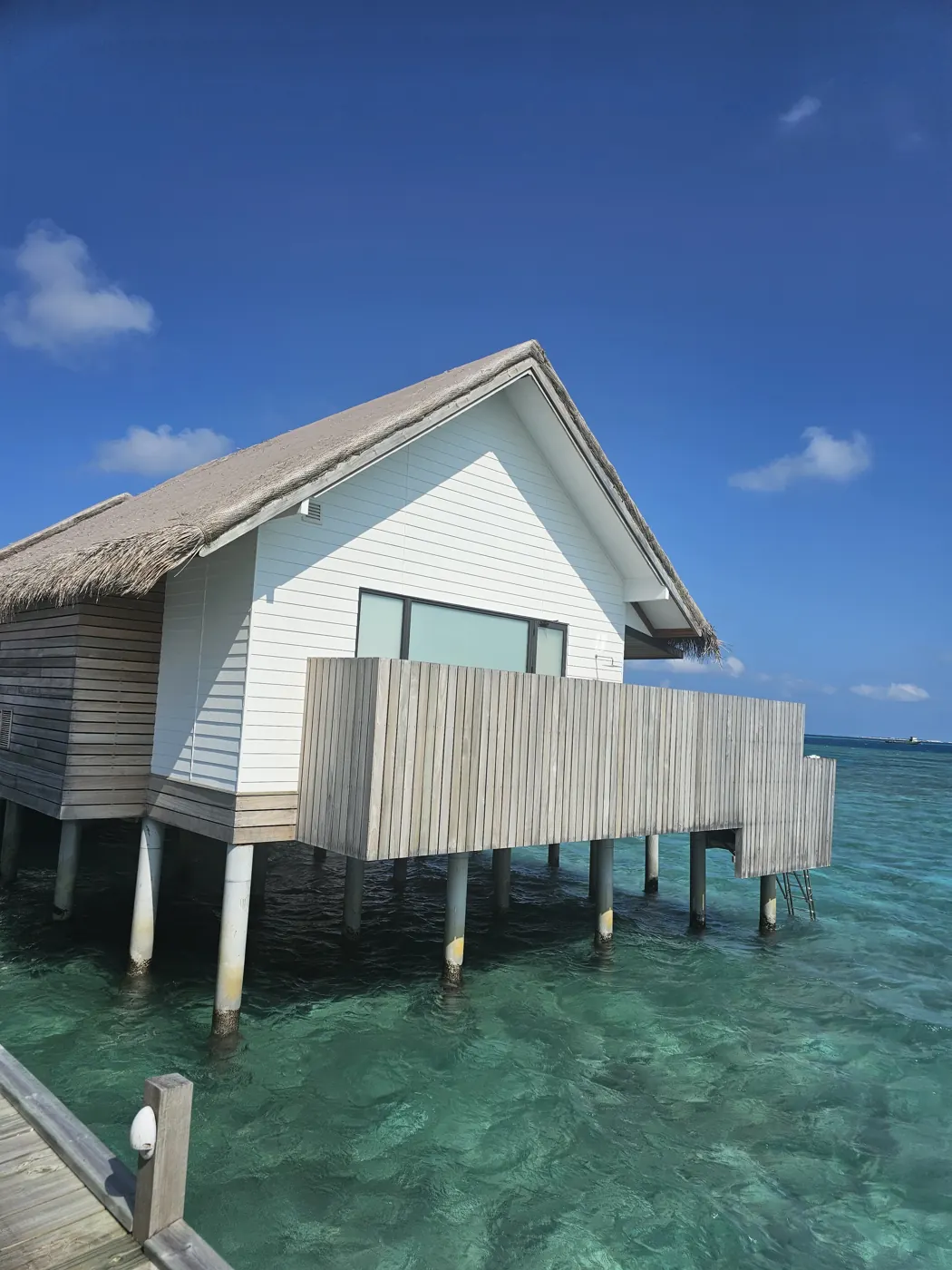A thatched overwater villa standing above clear shallow water in the Maldives